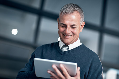 Middle aged man smiling as he types on his iPad.